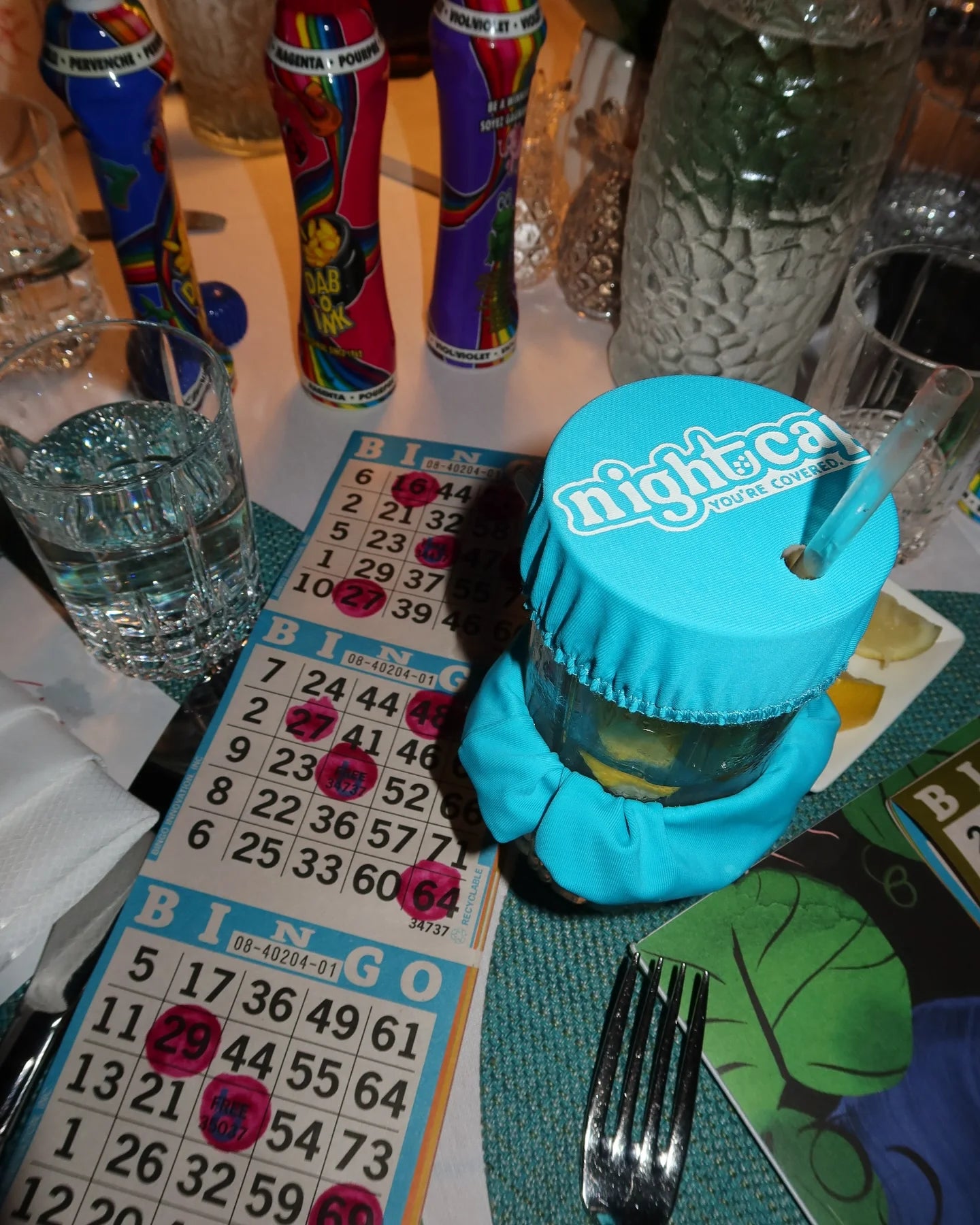 NightCap blue drink cover protecting a cocktail with a straw during a bingo night social event.