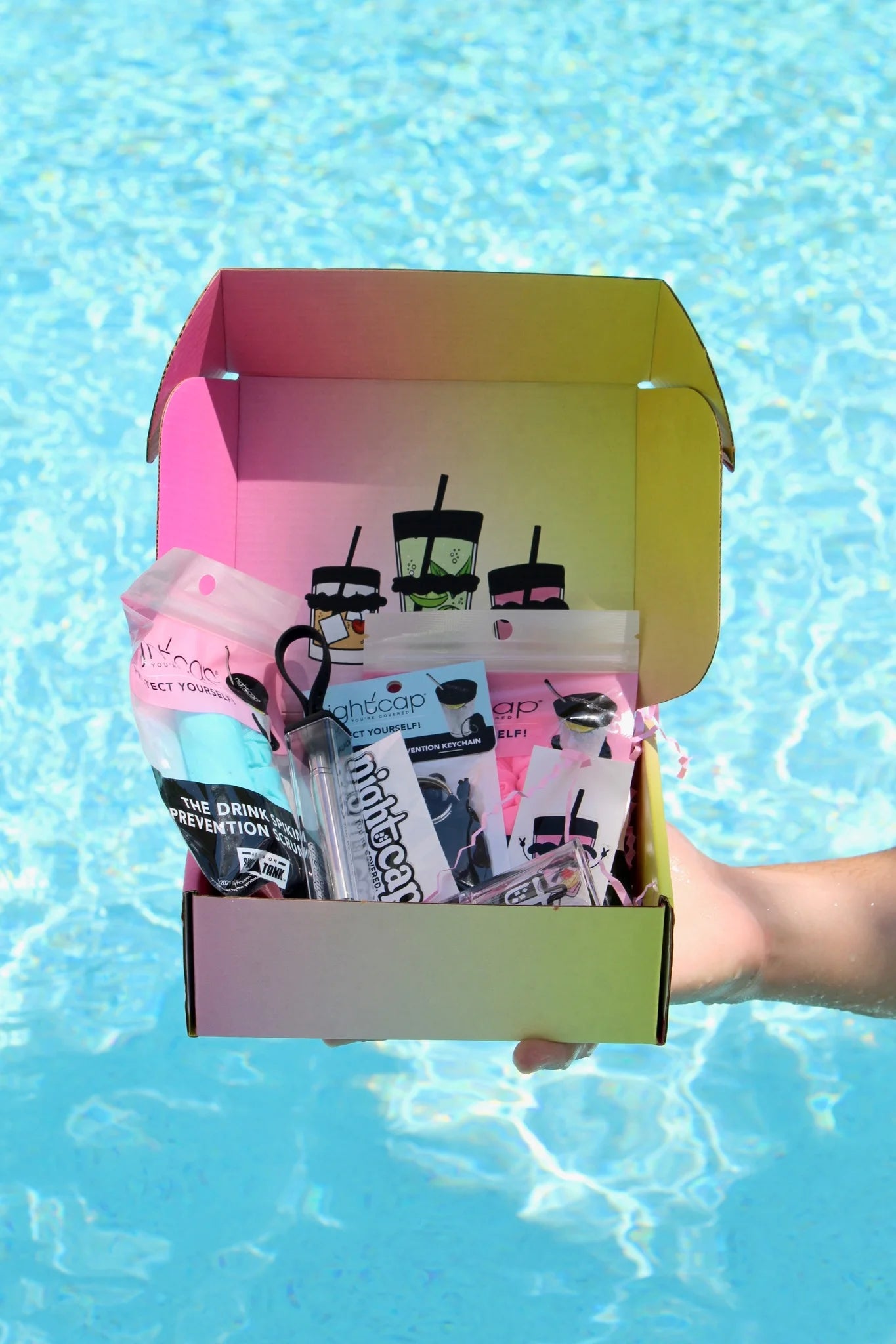 NightCap Gift Box featuring reusable drink spiking prevention scrunchies, keychain, bottle tops, keychain straw, shot glass, and stickers in gift-ready packaging.